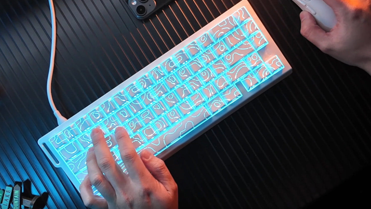 A person typing on a white mechanical keyboard with bright cyan backlighting illuminating a topographic line pattern on the keycaps