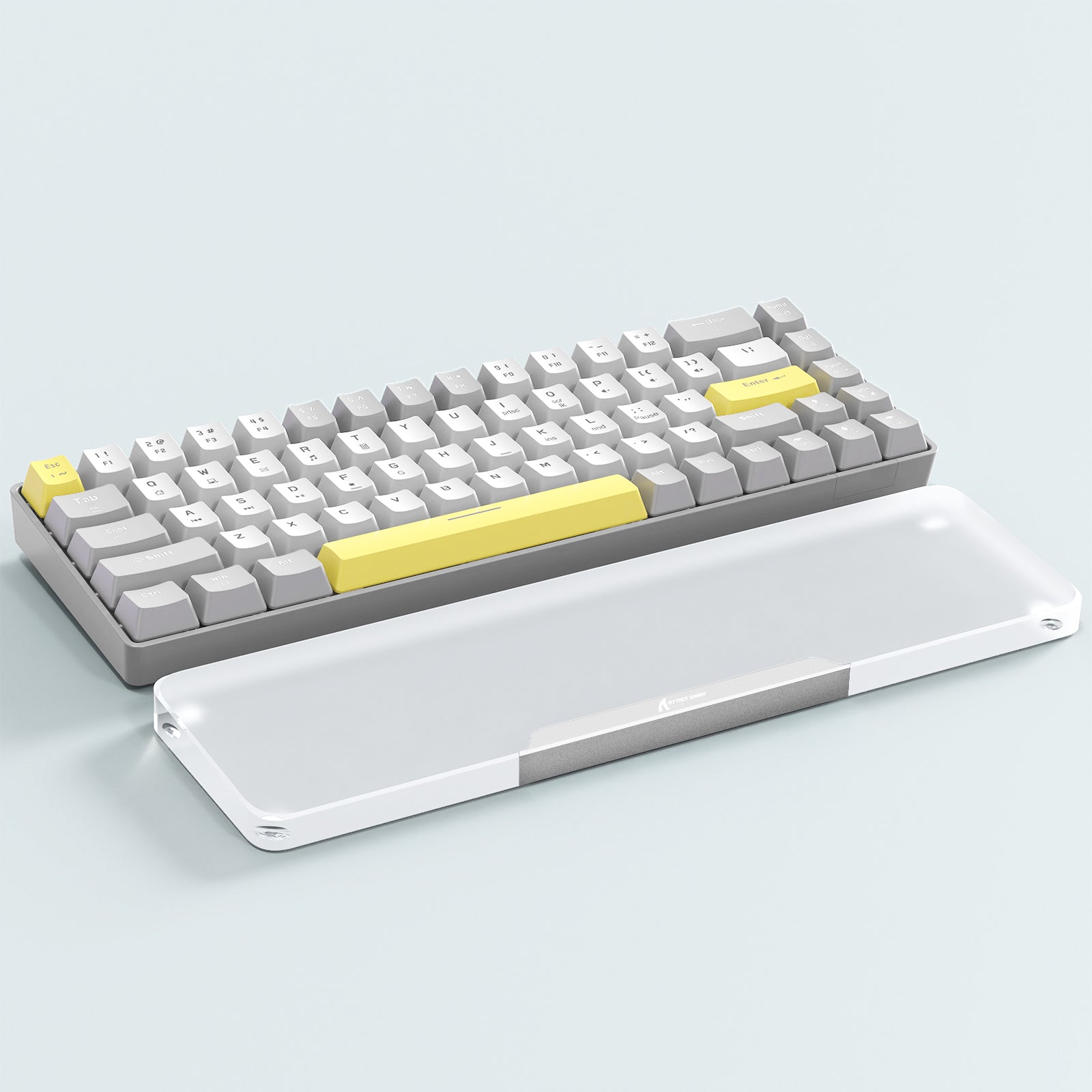 Mechanical keyboard with gray and yellow keycaps beside clear acrylic wrist rest.